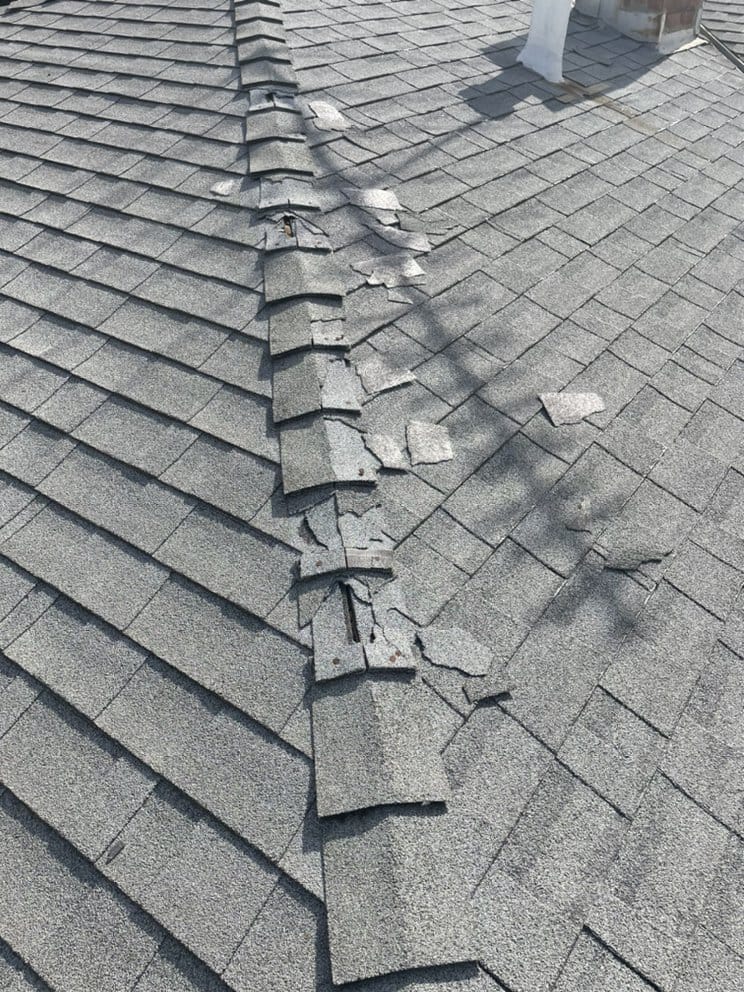 Close-up view of wind damage on roof shingles, showing lifted and missing pieces.